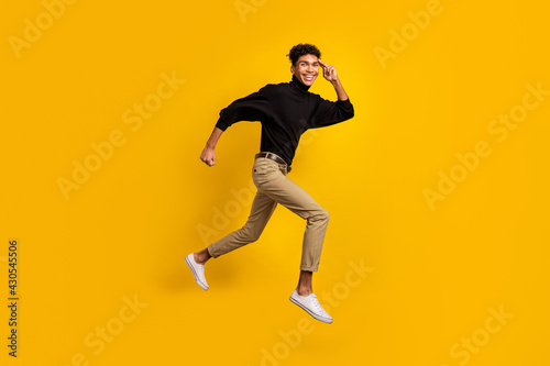 Full size profile photo of optimistic nice brunet guy run look wear black sweater trousers sneakers isolated on yellow background