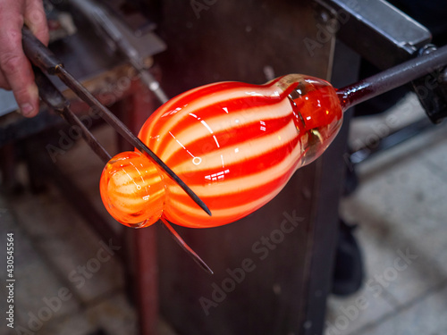Hands shaping melted glass with long knife jack. Art and craft worker molding