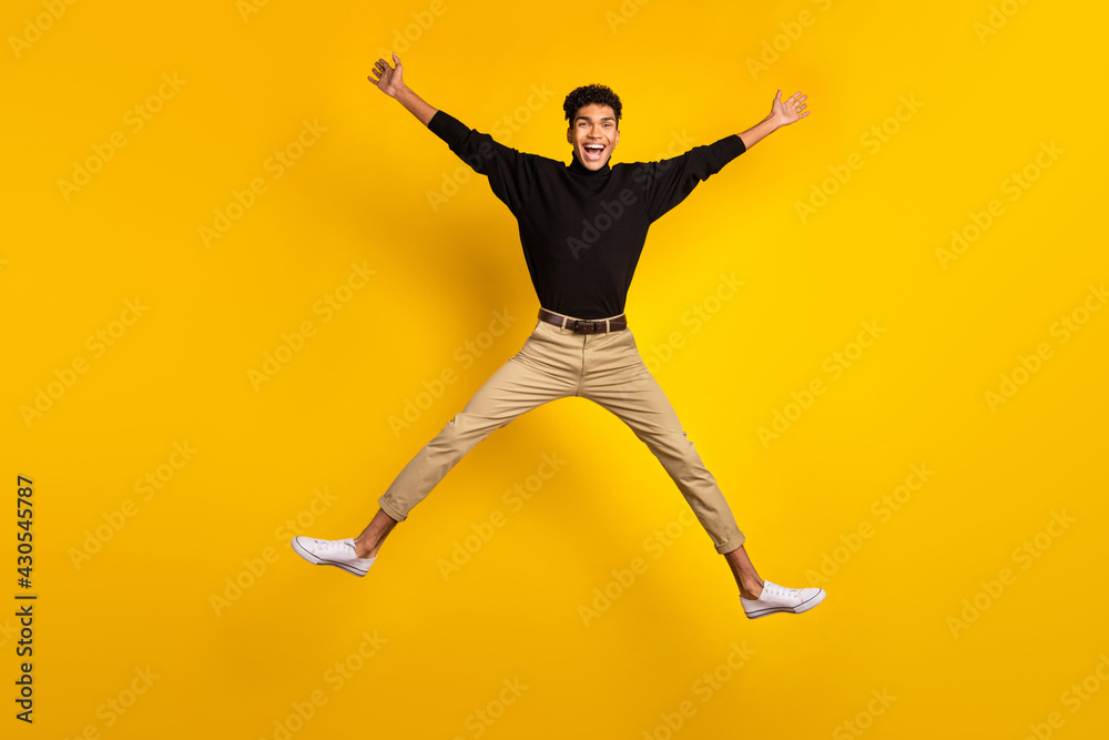 Photo of cute funny dark skin guy dressed black pullover jumping high like star isolated yellow color background