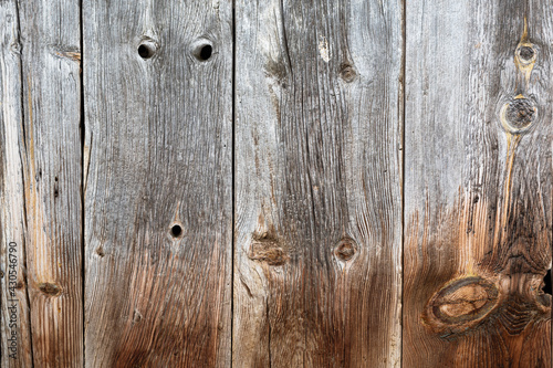Old dry wooden door with knots and holes. Vintage grey and brown cranny old wood texture. Antique natural wooden planks background template.