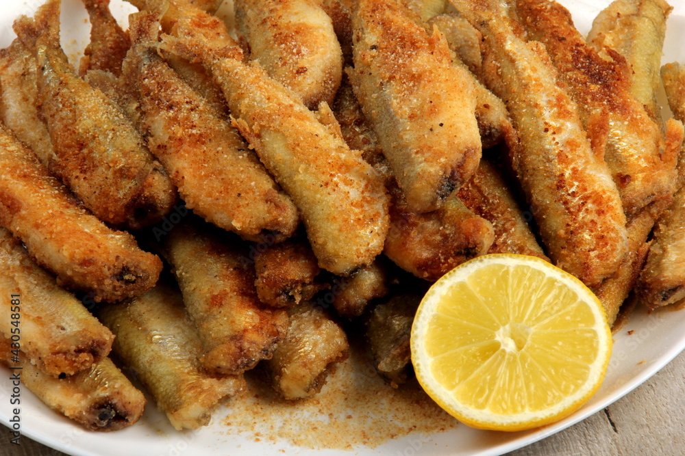 Small fried fish with breadcrumbs on a white plate with fresh lemon. Fried small fish in breading, close-up on a plate. horizontal view from above 