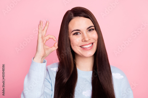 Photo of pretty adorable young lady dressed blue sweater smiling showing okey sign isolated pink color background