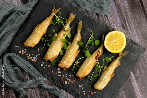 Foto fried breaded fish served on a black stone, decorated with fresh lemon, dark wooden background