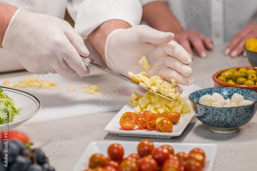 Male chef wearing gloves putting cut apples on a dish using his knife: selective focus