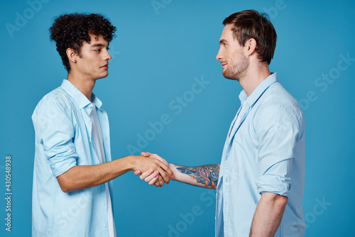 curly guy in a shirt stands next to a young man in a t-shirt on a blue background cropped view