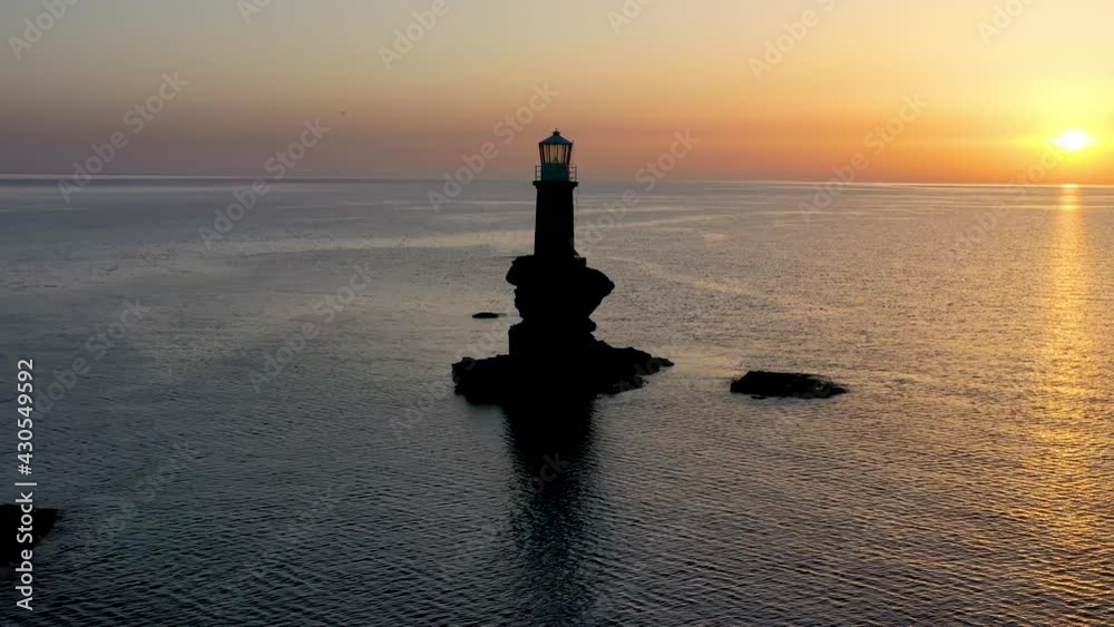 The lighthouse Tourlitis on a steep rock within the calm, mediterranean sea of Greece during summer sunrise, Andros island, Cyclades The lighthouse Tourlitis on a steep rock within the calm, mediterranean sea of Greece during summer sunrise, Andros island, Cyclades