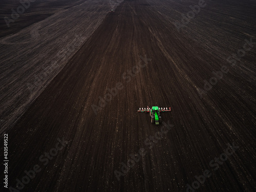 Aerial view of a modern green tractor seeding agricultural field , preparing land for sowing, spring, drone video.