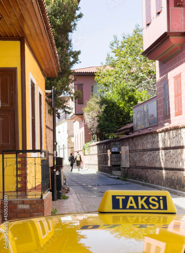 Yellow Taxi cab roof sign with TAKSI turkish word. Auto was parking on the narrow old Antalya street. Unfocused couple walking away on the background. Traveling in Turkey concept image. photo