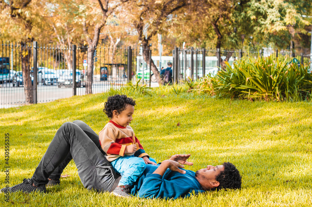 young father and black-skinned son, lying in a park, interacting, playing, father's day concept