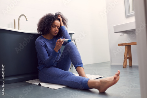 Disappointed Woman Sitting On Floor In Bathroom At Home With Negative Home Pregnancy Test photo