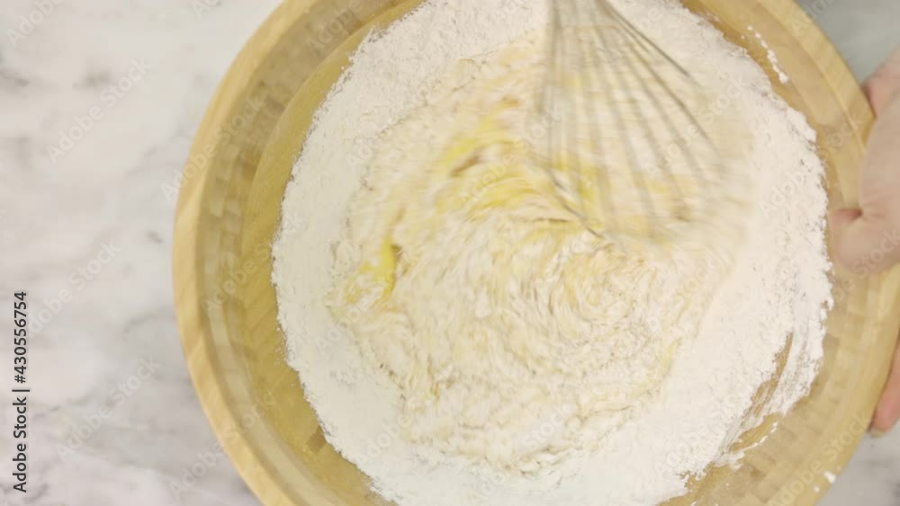 Female hands stir flour with beaten eggs to make a sponge cake. Mixing ingredients in bowl on a white table. Cooking a sponge cake.