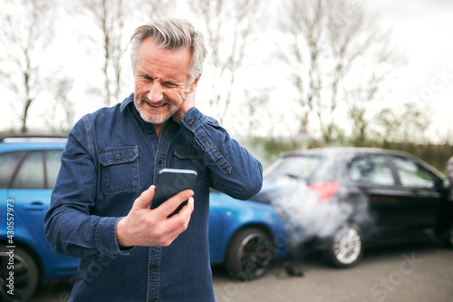 Senior Male Driver With Whiplash Calls Car Insurance Company On Mobile Phone After Traffic Accident