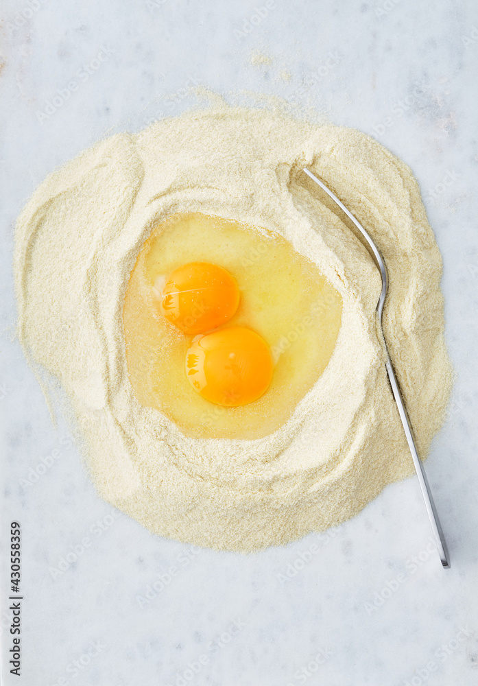 A egg sits in a well formed in the middle of freshly milled flour. The egg and flour will be combined to make fresh pasta. A egg sits in a well formed in the middle of freshly milled flour. The egg and flour will be combined to make fresh pasta.