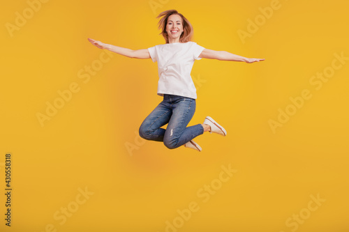 Smiling positive girl jumping hands wings inspiration on yellow background