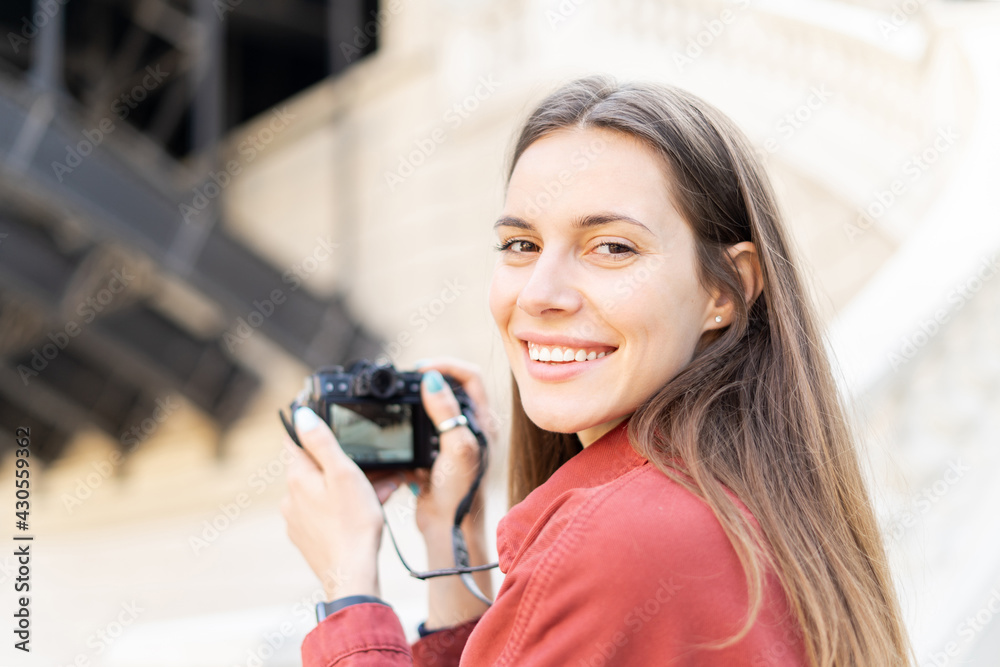 Portrait of a charming young woman ready to make a picture of her mirorless vintage camera, while looking in the frame with her beautiful smile outdoors