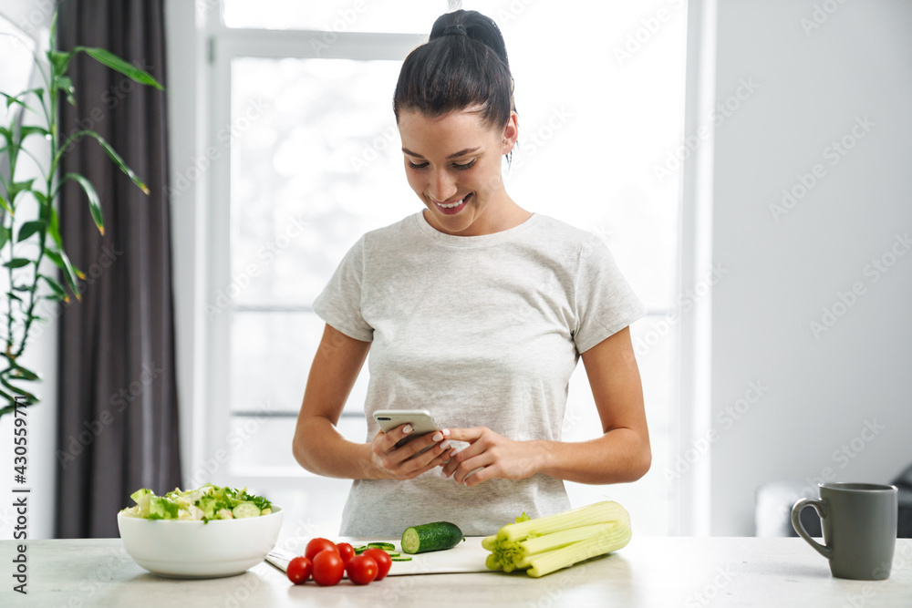 European smiling woman using mobile phone and making salad European smiling woman using mobile phone and making salad