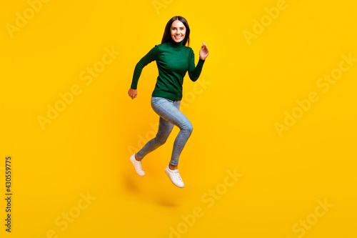 Full size photo of nice optimistic brunette lady jump wear green sweater jeans sneakers isolated on bright yellow color background © deagreez