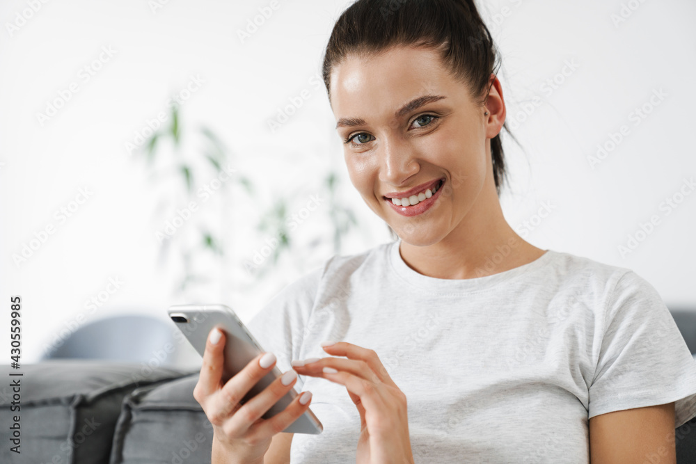 European smiling woman using mobile phone while sitting on couch European smiling woman using mobile phone while sitting on couch