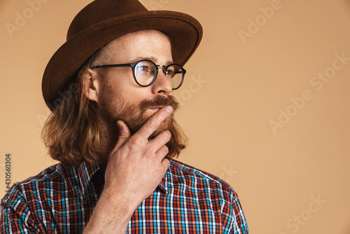 Thinking ginger man wearing eyeglasses and hat looking aside