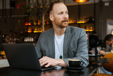 White bearded man in jacket using laptop in cafe outdoors
