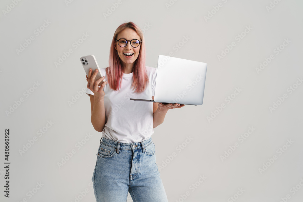 Young woman smiling while posing with laptop and cellphone Young woman smiling while posing with laptop and cellphone