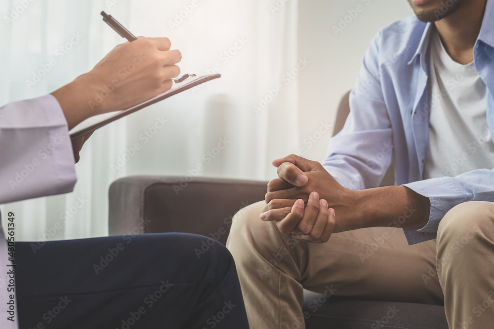Asian young man, male has mental symptoms which must have been therapy and stress, sitting on couch to consult to psychologist during the session taking notes to find out how to treat the therapist. Asian young man, male has mental symptoms which must have been therapy and stress, sitting on couch to consult to psychologist during the session taking notes to find out how to treat the therapist.