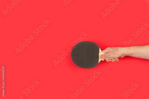 Mano de hombre sosteniendo una raqueta de ping pong  sobre un fondo rojo liso y aislado. Vista de frente y de cerca. Copy space photo