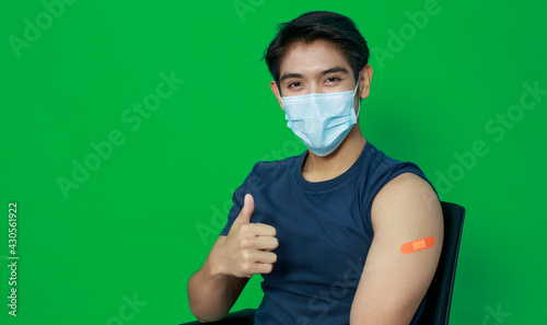 Asian young man wearing protective hygiene mask trust and confident show arms with bandage plaster after getting Coronavirus or Covid-19 vaccine injection. Idea for safe and drug allergy free