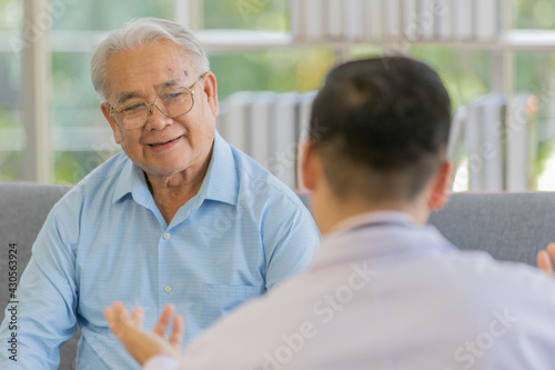 Wallpaper Mural An old fat male patient with gray white hair wearing light blue shirt and brown pants sitting on sofa and discussing about health with a young doctor with black hair wearing white lab coat Torontodigital.ca