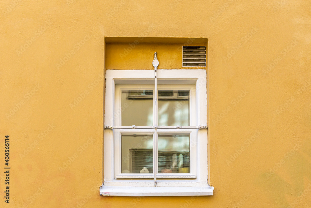 Small window on yellow facade with fence