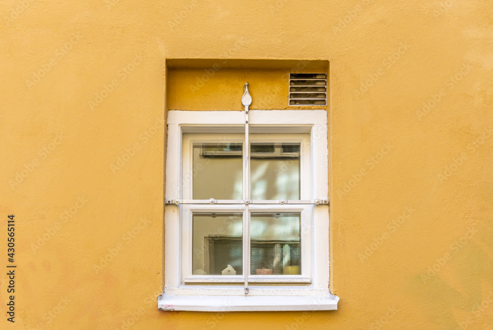 Fototapeta premium Small window on yellow facade with fence