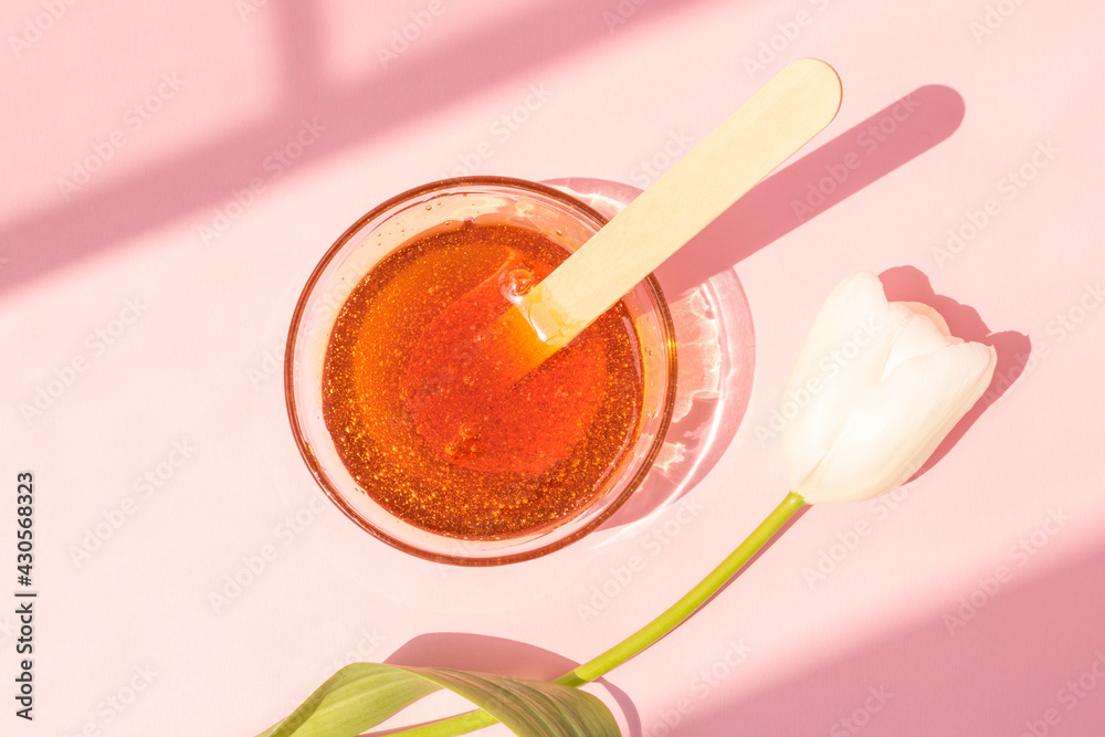 Shugaring paste in a glass bowl on a pink background. Hair removal, epilation, wooden spatula for sugaring paste, tulip. Shugaring paste in a glass bowl on a pink background. Hair removal, epilation, wooden spatula for sugaring paste, tulip.