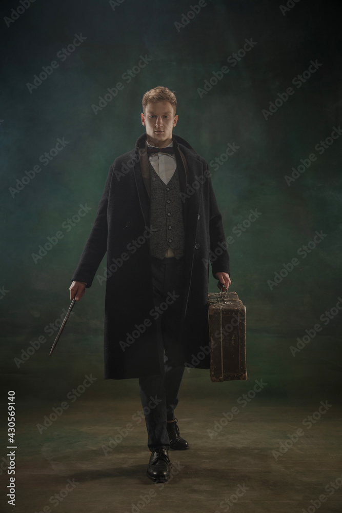 Fototapeta premium Young man in art action isolated on dark green background. Retro style, comparison of eras concept.