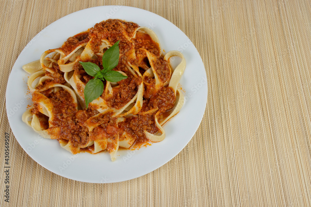 Tasty Pasta with bolognese sauce and basil leaves. Pasta served on a plate on a bamboo mat. Italian gastronomy photography. Photo with space for text on the right. Tasty Pasta with bolognese sauce and basil leaves. Pasta served on a plate on a bamboo mat. Italian gastronomy photography. Photo with space for text on the right.