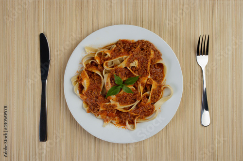 Tasty Pasta with bolognese sauce and basil leaves. fork on the right and knife on the left. bamboo mat background. Top view photo.
