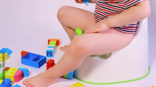 A little boy sits on a pot and plays with multi-colored designer cubes. Get used to the pot.
