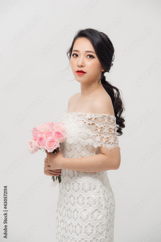 Young beautiful pretty Asian girl standing and holding pink roses over white background. Young beautiful pretty Asian girl standing and holding pink roses over white background.