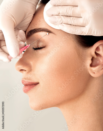 Lifting eyebrow lines using mesothreads. Needle with mesothreads near a female face for contour facial lifting procedure photo