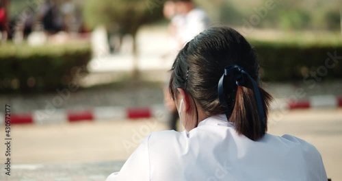 Back view slow motion scene of an Asian female high school student in a white school uniform sitting alone , put on the earphones while waiting for the pickup to go home after school. photo