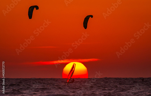Under the sun. Two kites and windsurfer at sunset.