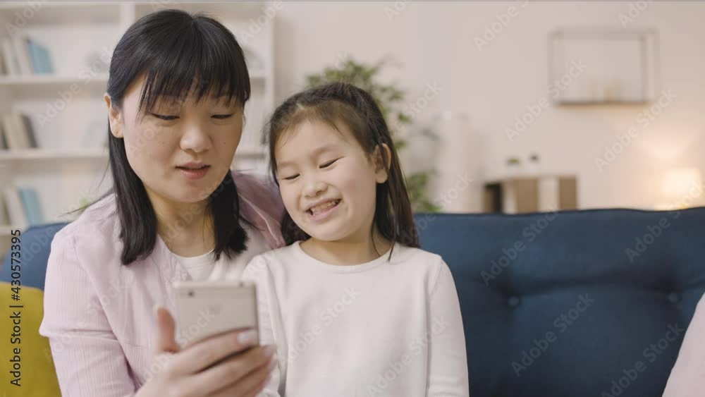 Asian woman and little girl looking at smartphone, using mobile app together Asian woman and little girl looking at smartphone, using mobile app together