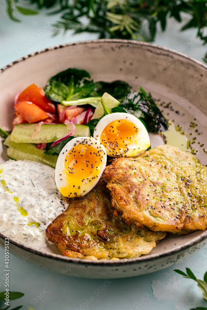 Side view on zucchini fritters with eggs sauces and vegetables Side view on zucchini fritters with eggs sauces and vegetables