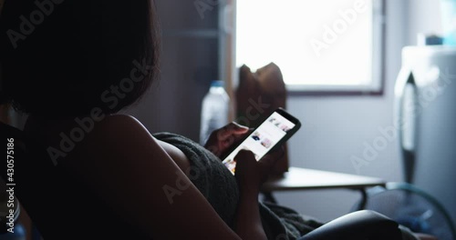 A lonely poor working-age woman rented an apartment, kept in a narrow room, dimly lit, there was light from the window, fast food on the table, wearing a towel, watch social media on a mobile phone.