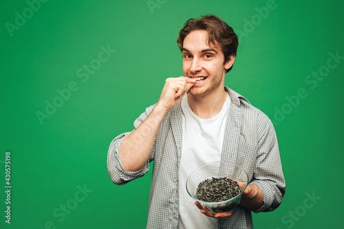 Young man eats sunflower seeds, isolated on green background