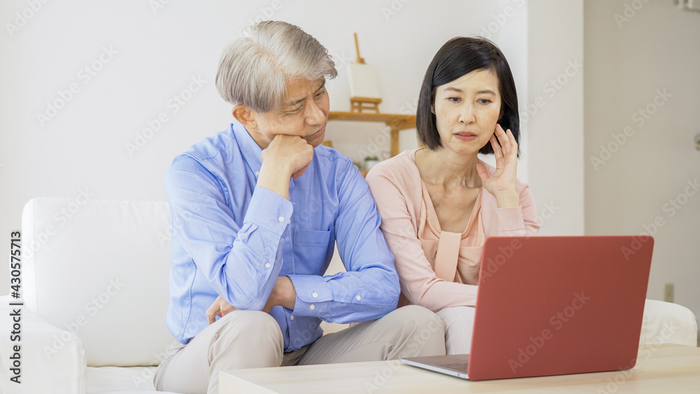 パソコンをしながら考え事をする中高年夫婦 パソコンをしながら考え事をする中高年夫婦