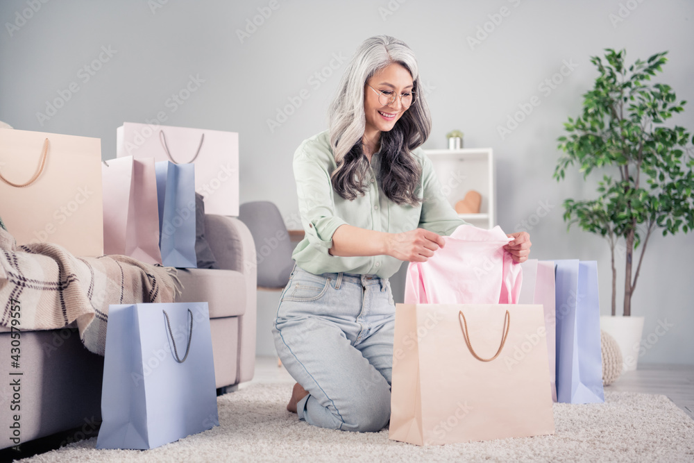 Full body portrait of cheerful aged person it on knees hands taking clothing from bag toothy smile indoors Full body portrait of cheerful aged person it on knees hands taking clothing from bag toothy smile indoors