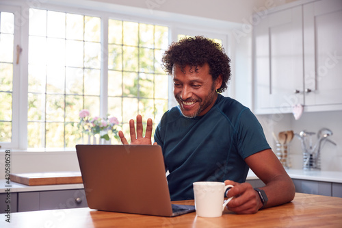 Tableau sur toile Mature Man At Home In Kitchen Waving As He Makes Video Call On Laptop Computer