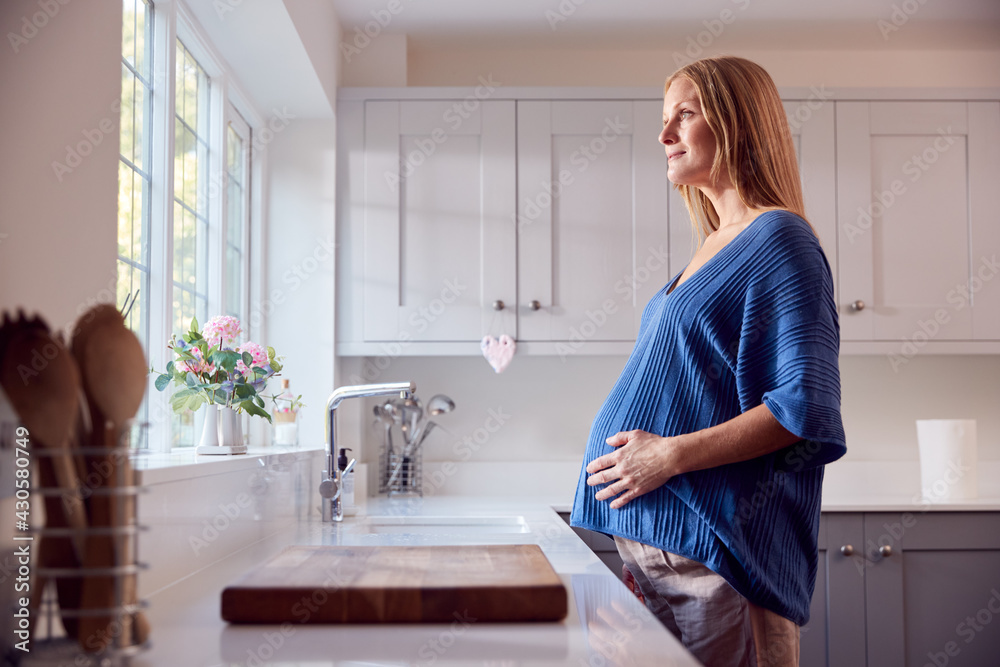 Smiling Pregnant Woman Standing By Kitchen Window Touching Stomach Smiling Pregnant Woman Standing By Kitchen Window Touching Stomach