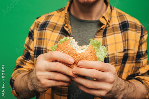 Close up young man holds burger, isolated on green background