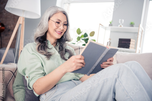 Side profile photo portrait of old lady sitting on sofa after work reading book spending free time